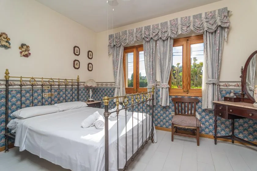 A bedroom with a metal bed, patterned wall tiles, and windows with draped curtains.