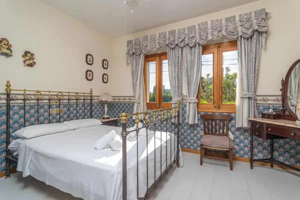 A bedroom with a metal bed, patterned wall tiles, and curtained windows.