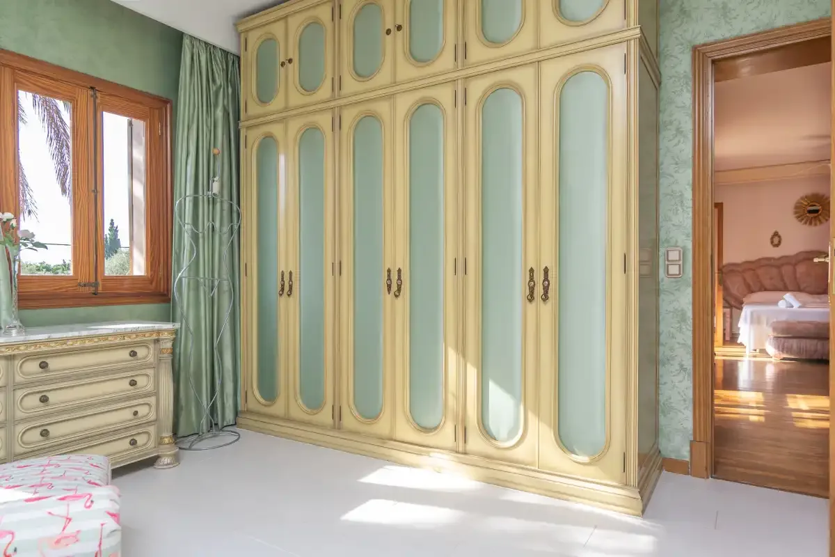 A bedroom with a large wardrobe, a window, and a doorway to another room.