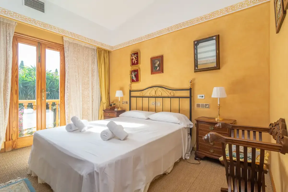 A bedroom with a double bed, bedside lamps, and glass doors opening onto a balcony.