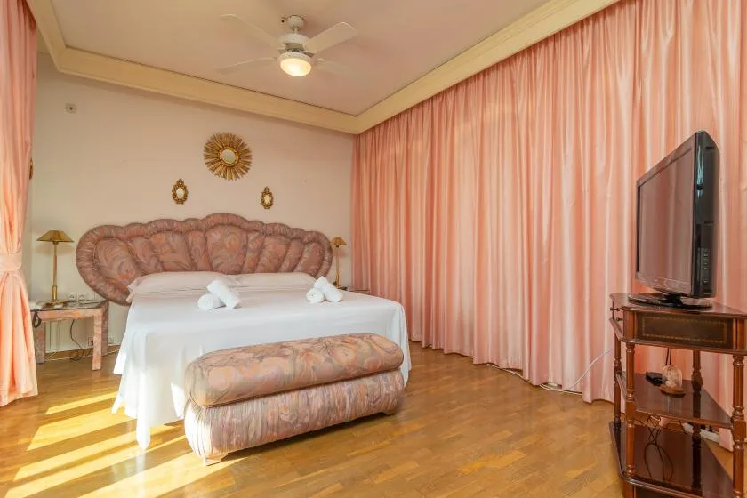 A bedroom with a bed, pink curtains, and a television.