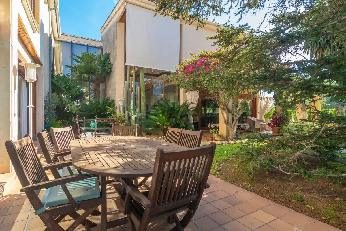 A paved courtyard with a wooden outdoor dining table and surrounding greenery.