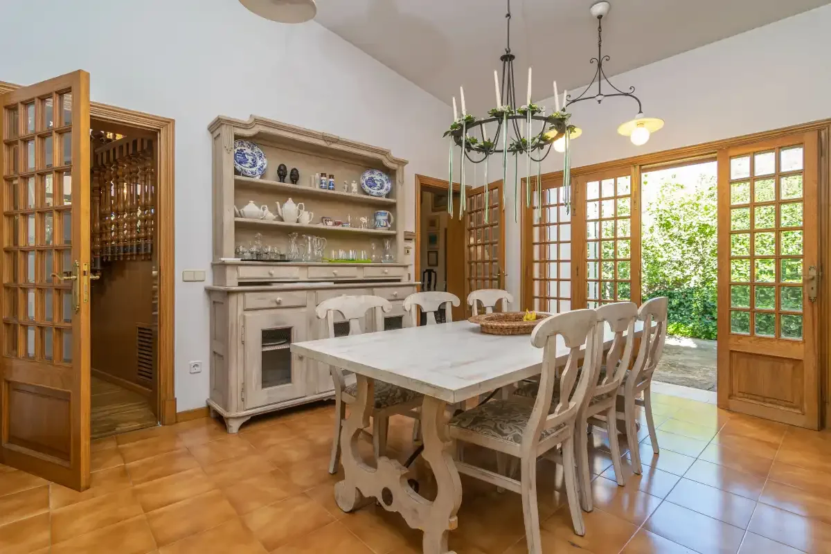 A dining room with a long table and wooden chairs beside open doors.