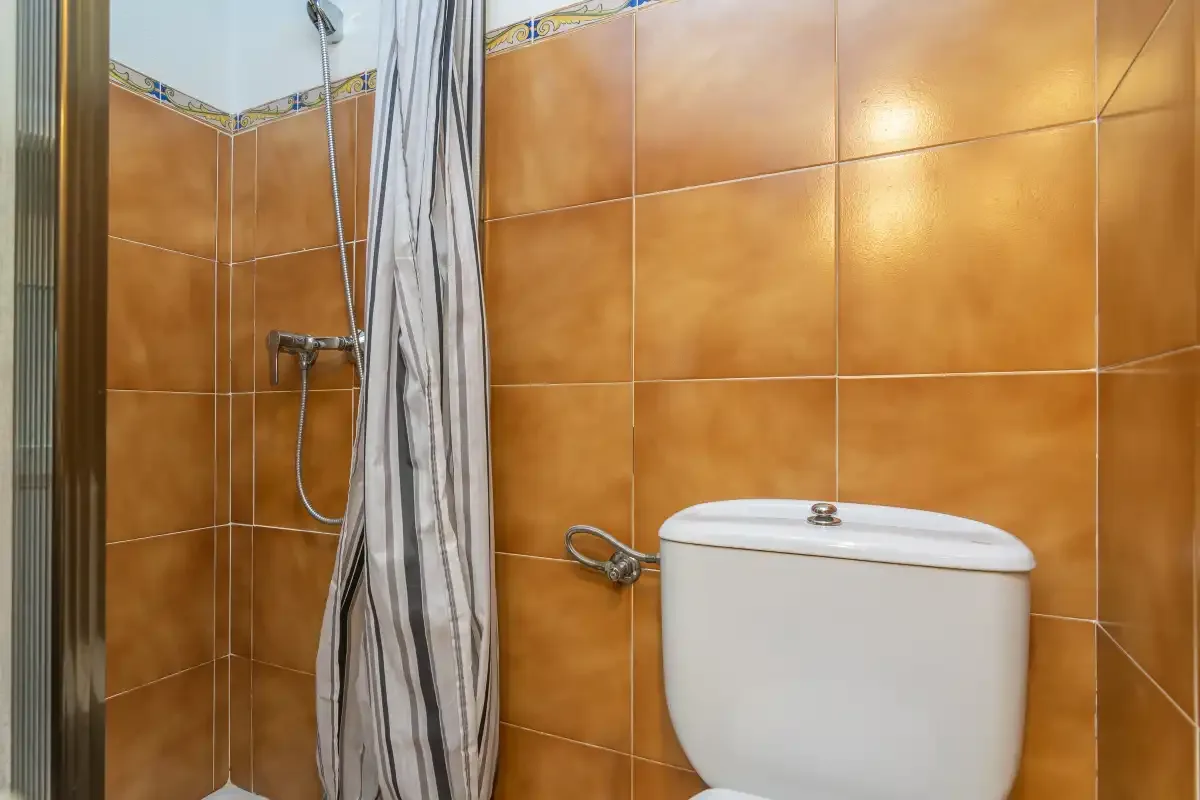 A bathroom with orange tiled walls, a shower, and a toilet.
