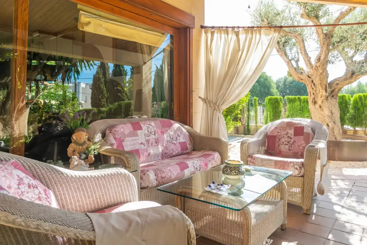 A bright patio seating area with wicker furniture and curtains opening onto a garden.