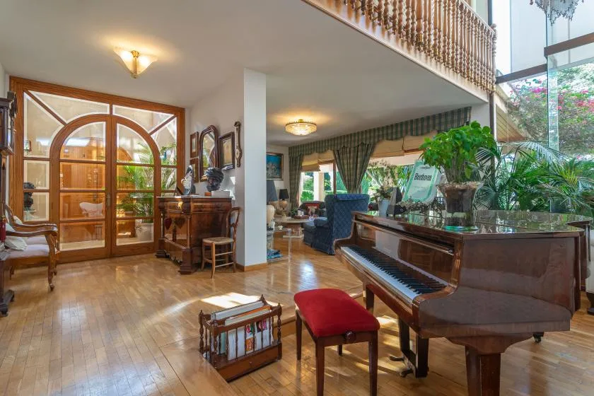 A spacious living room with a grand piano and large arched wooden doors.