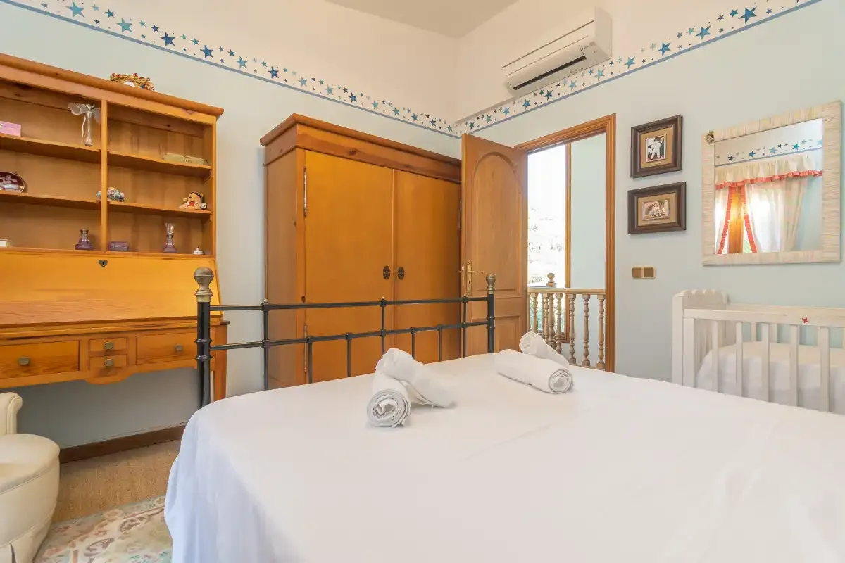 A bedroom with a neatly made bed, wooden wardrobe, and wall-mounted air conditioner.