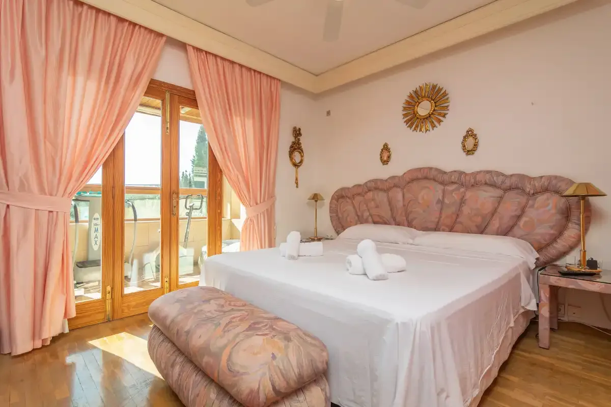 A bedroom with a neatly made bed and peach curtains beside the windows.