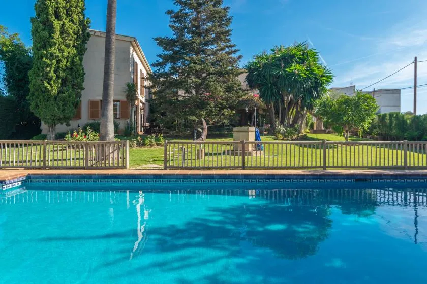 A swimming pool sits beside a fenced garden with trees and shrubs.