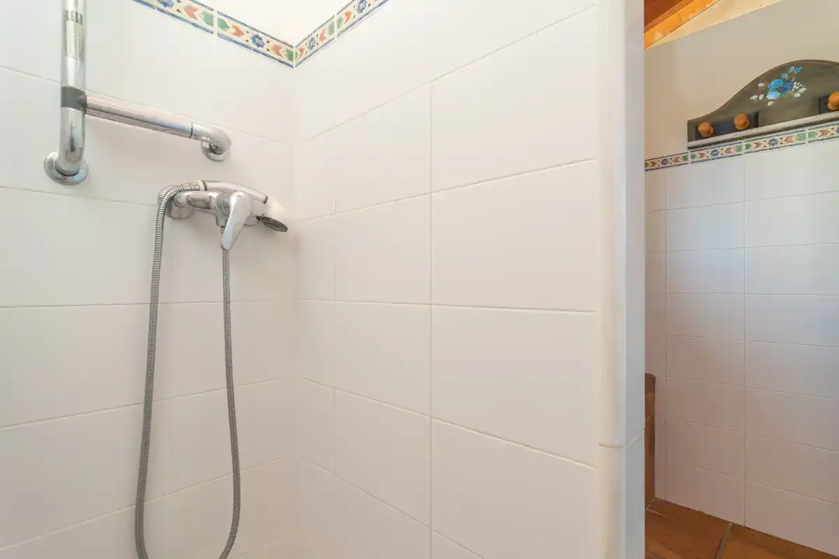 A tiled bathroom shower with a handheld showerhead and wall-mounted fixtures.