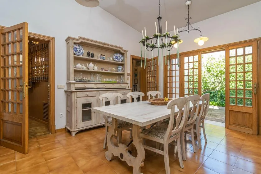 A dining room with a long table and wooden chairs beside open glass doors.