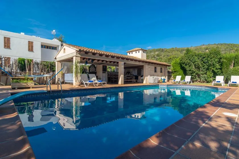 An outdoor swimming pool beside a covered patio and lounge seating.