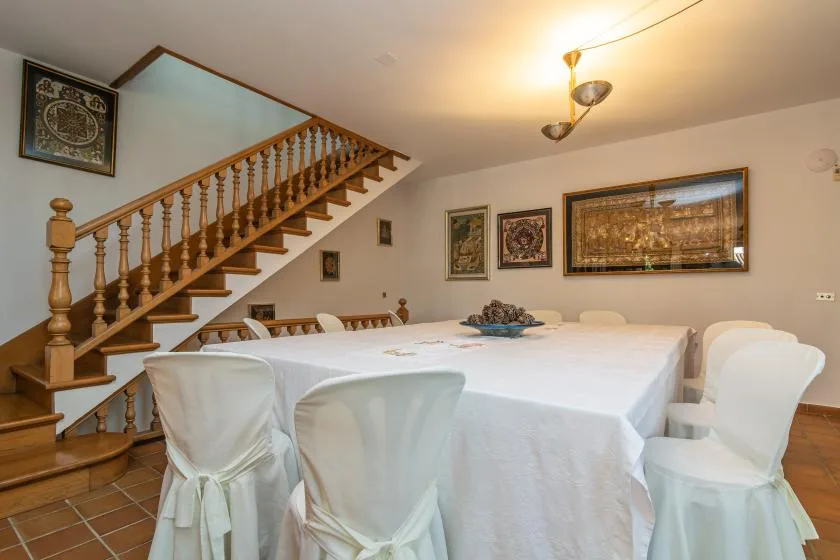 A dining room with a large table covered in white cloth and surrounded by covered chairs.