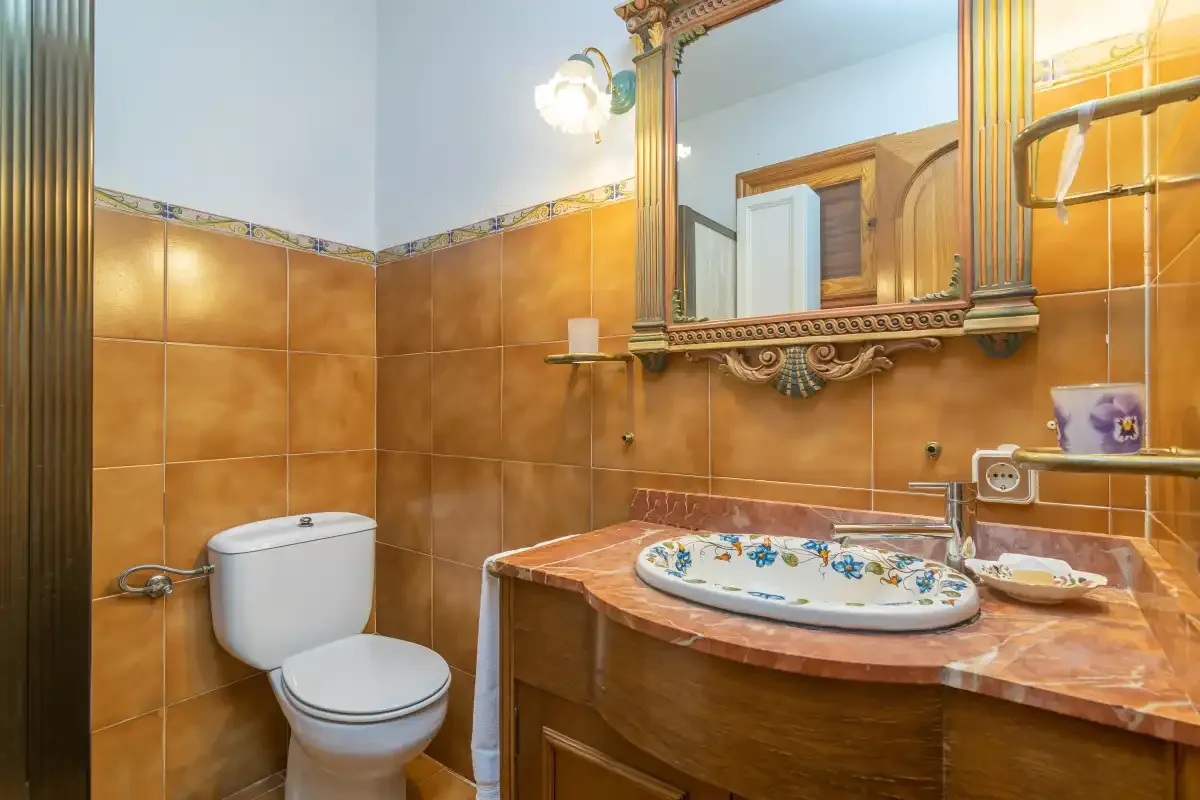 A tiled bathroom with a toilet and a sink beneath a large mirror.