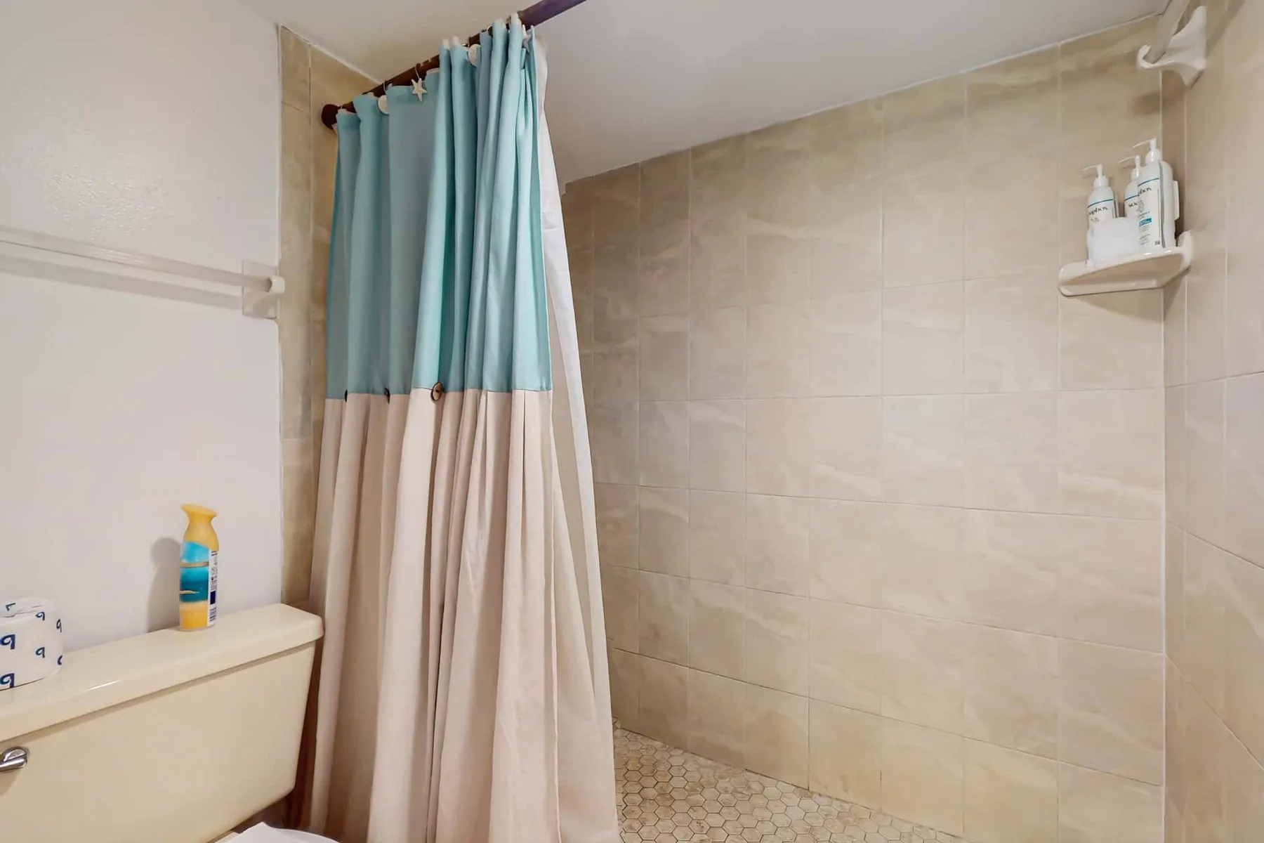 A tiled bathroom shower with a two-tone curtain and a small corner shelf.