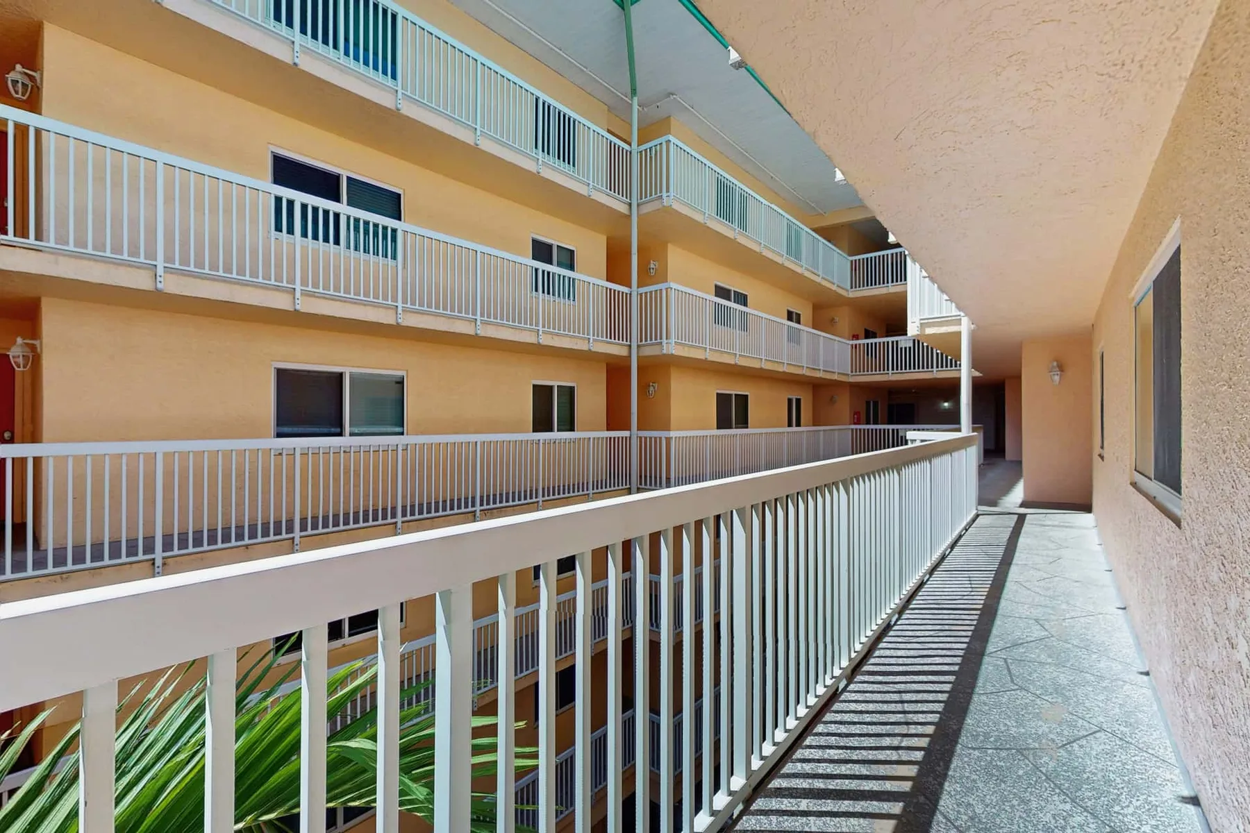 An open-air building corridor with metal railings and apartment doors.