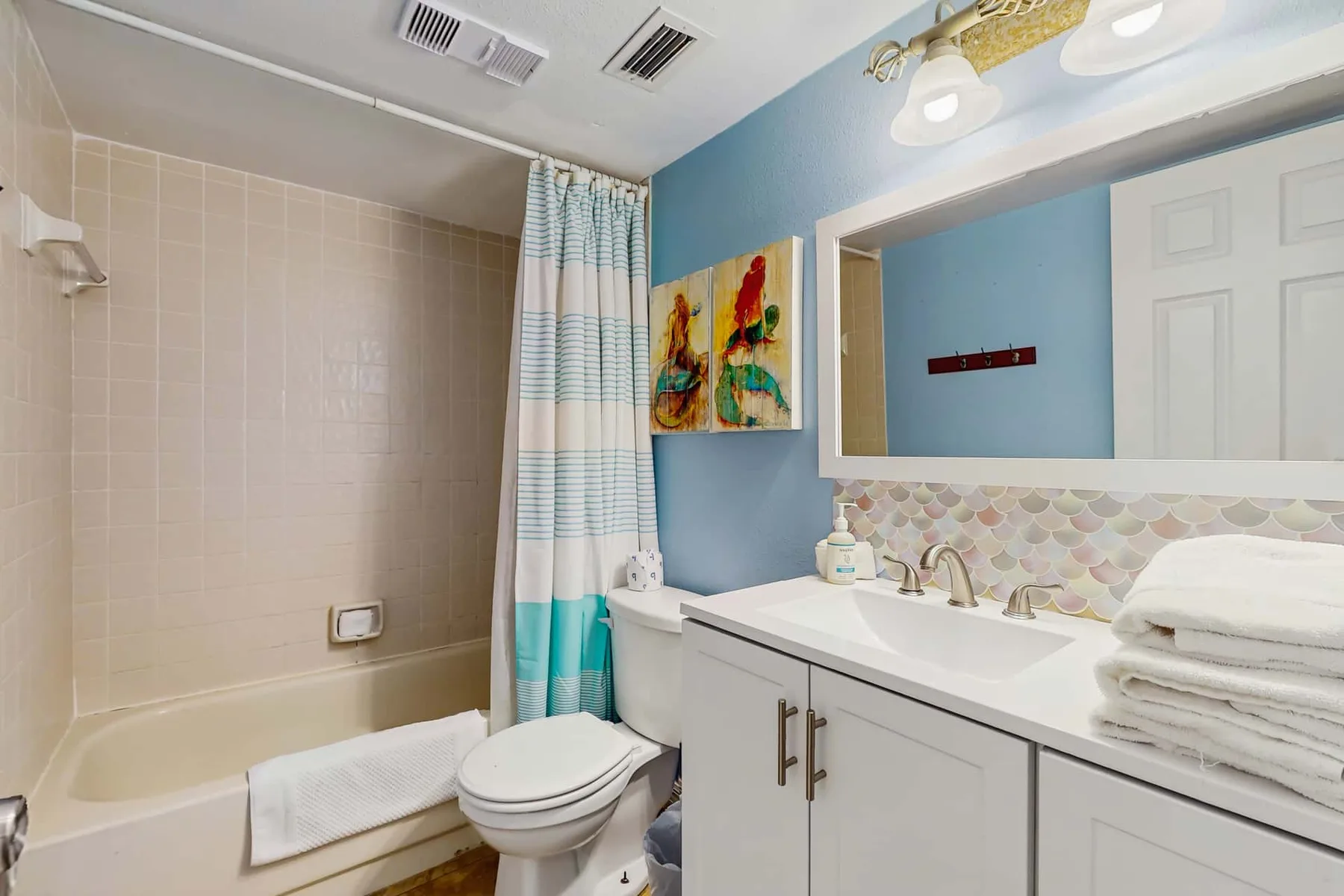 A bathroom with a bathtub, shower curtain, toilet, and vanity.