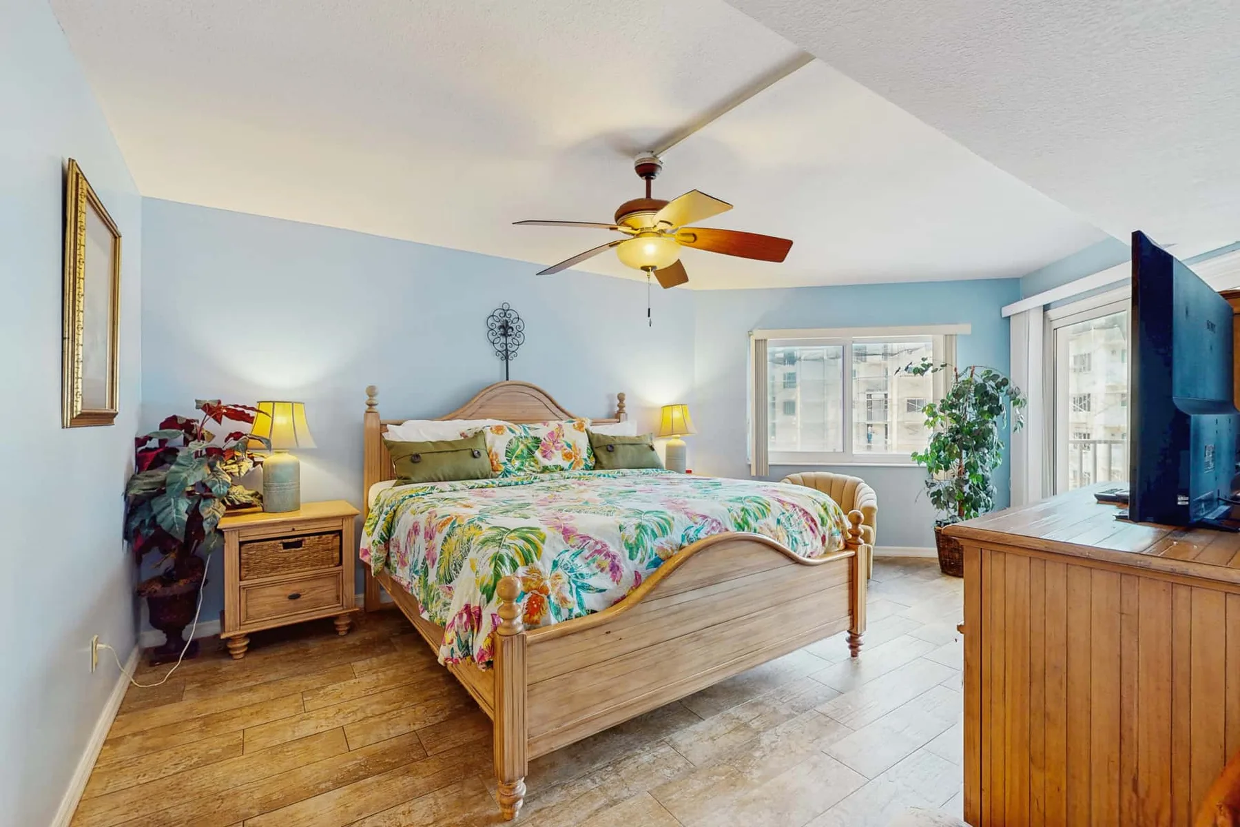 A bedroom with a wooden bed, colorful floral bedding, and large windows.