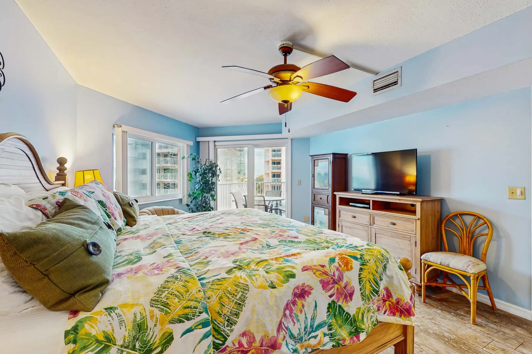 A bedroom with a bed covered in colorful floral bedding and a television.