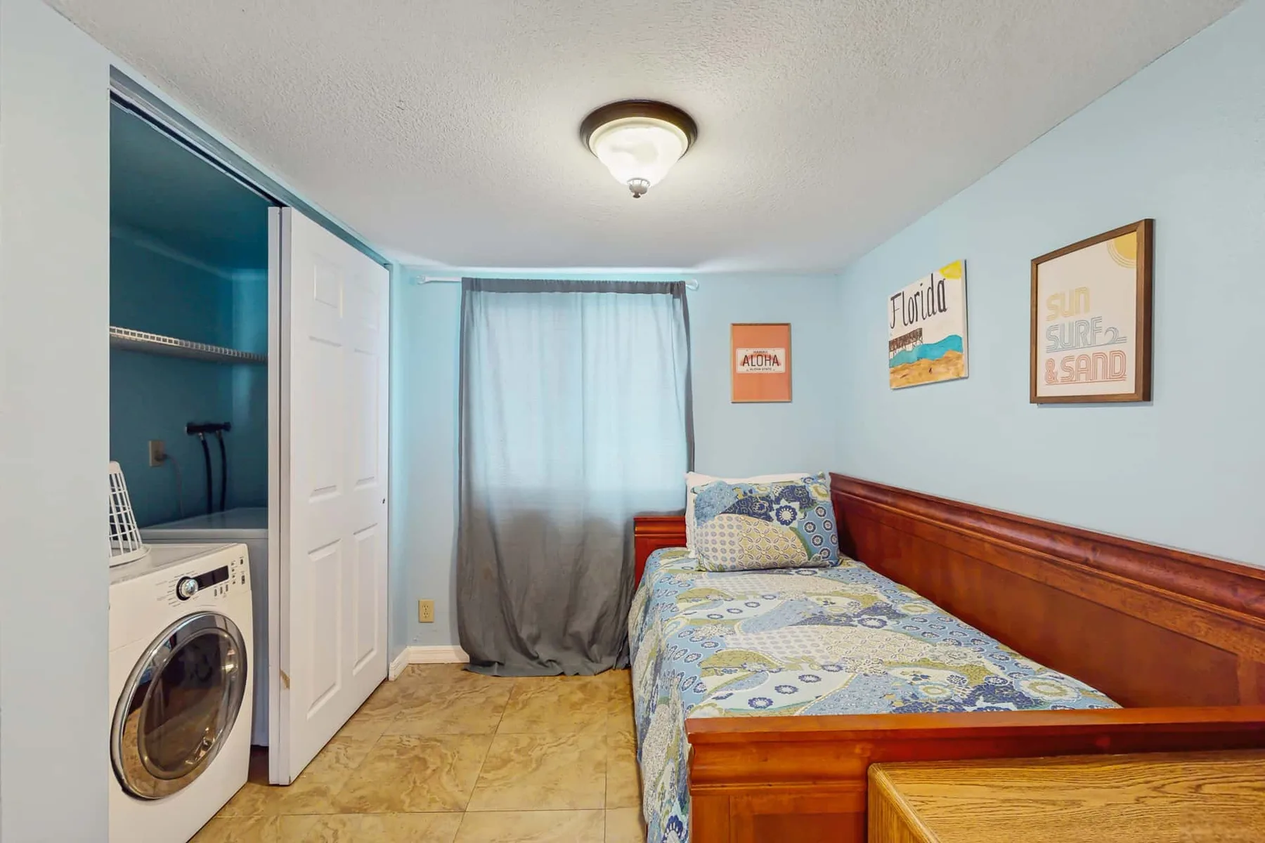 A bedroom with a single bed, a curtained window, and a laundry area.
