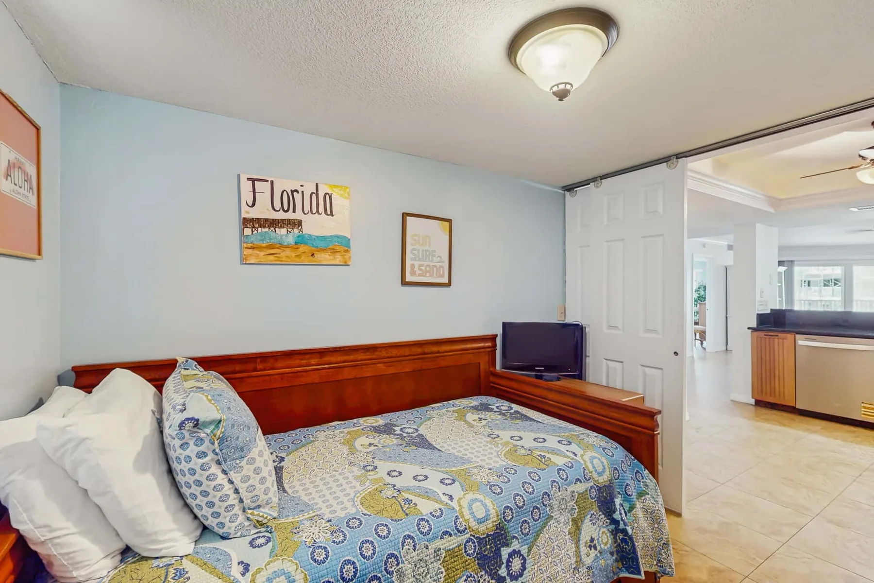 A bedroom with a patterned bedspread and an adjoining open kitchen area.