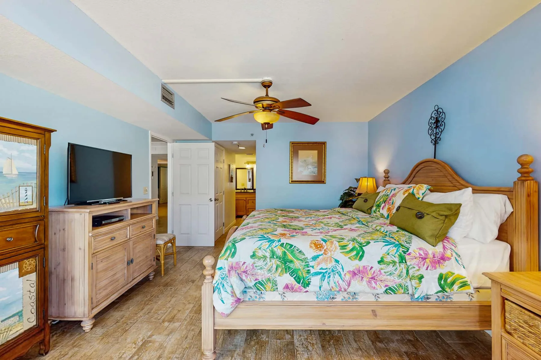 A bedroom with a wooden bed dressed in colorful floral bedding.