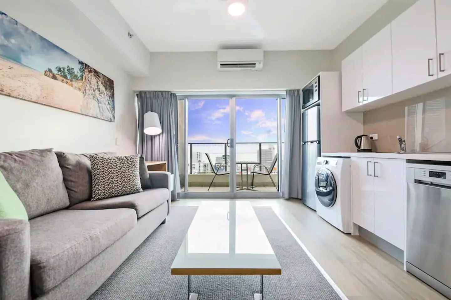 Una luminosa sala de estar da a un balcón, con un sofá y una cocina compacta.