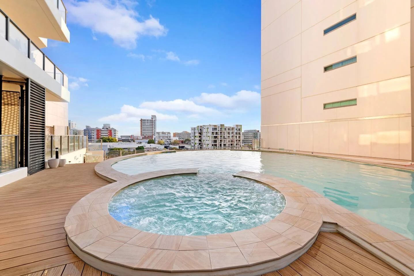 Una piscina al aire libre en una azotea, con un spa circular y tarima de madera.