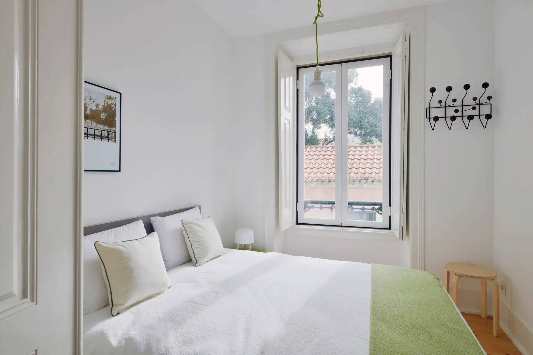 A bright bedroom with a neatly made bed and a window overlooking rooftops.