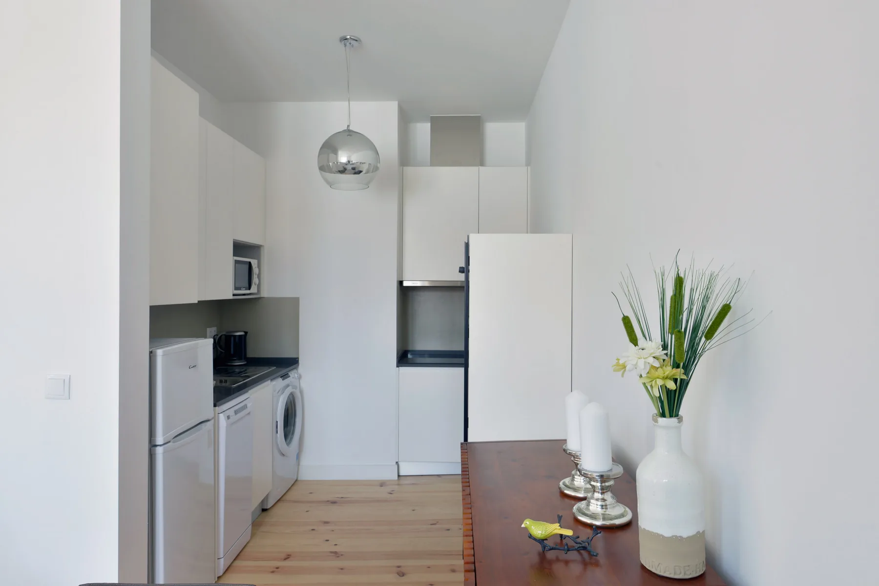 A compact kitchen with white cabinets, appliances, and a wooden dining table.