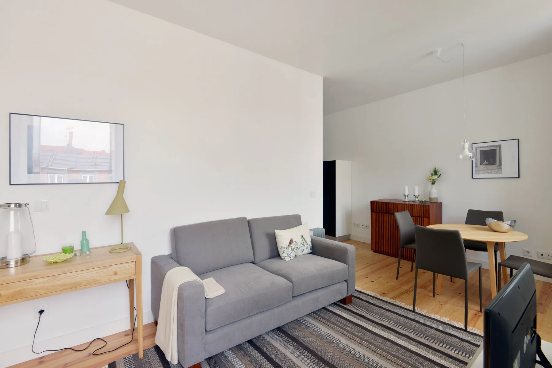 A living and dining area with gray seating, a wooden table, and a striped rug.