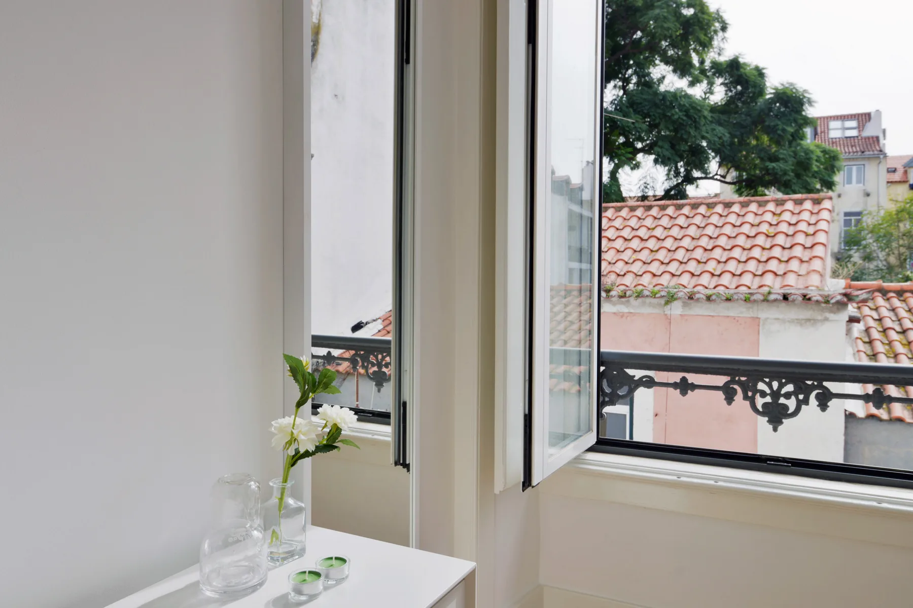 A bright interior beside open windows overlooking nearby rooftops and trees.