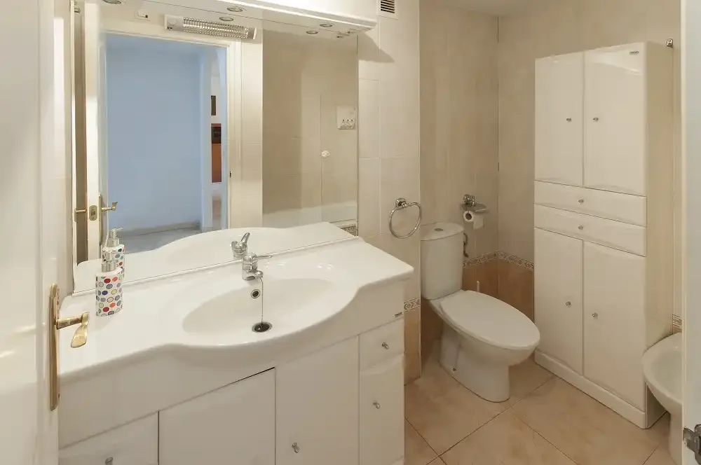 Un baño con lavabo, espejo e inodoro.