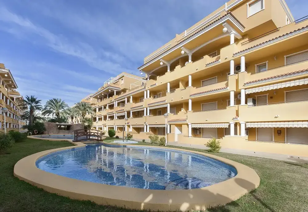 Una piscina al aire libre está frente a un edificio de apartamentos de varias plantas.