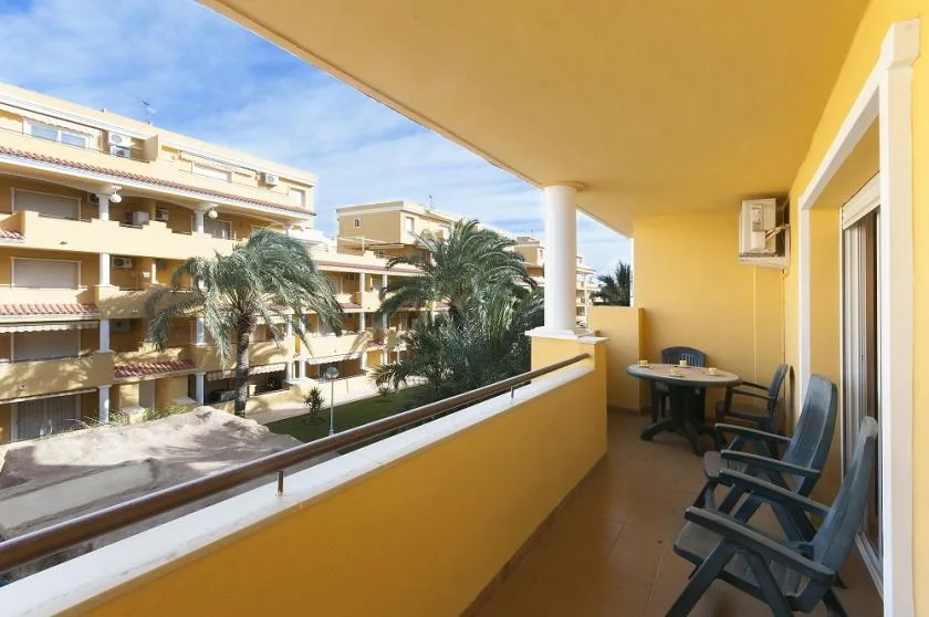 A covered balcony with outdoor seating overlooks nearby apartment buildings and palm trees.