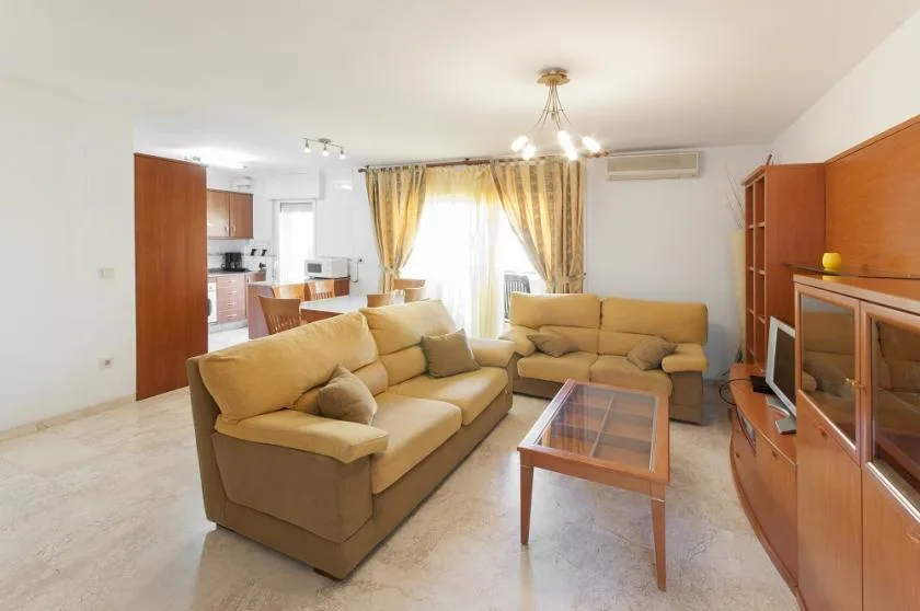 A living room with beige seating, a glass coffee table, and curtains by the window.