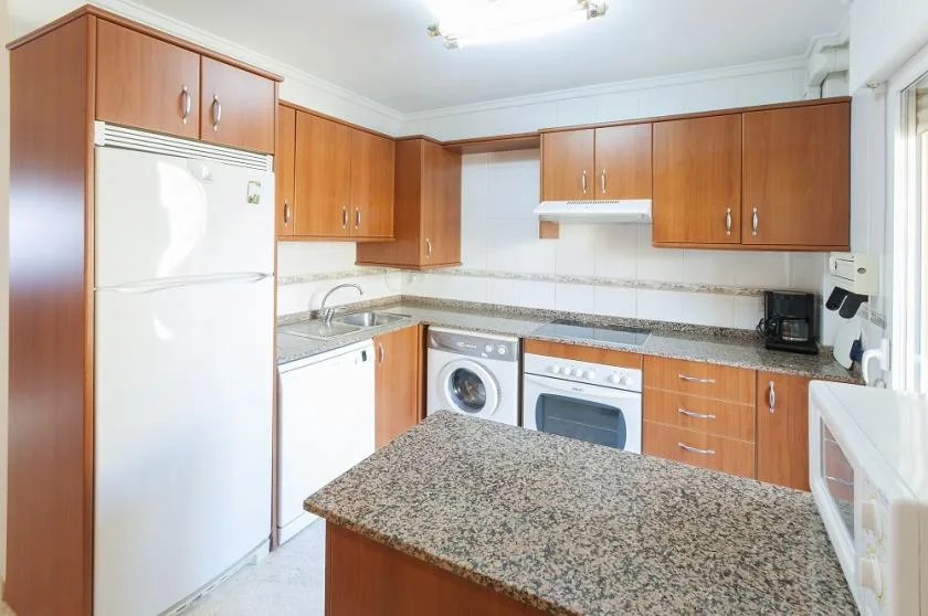Una cocina luminosa con gabinetes de madera, un refrigerador y una encimera central.