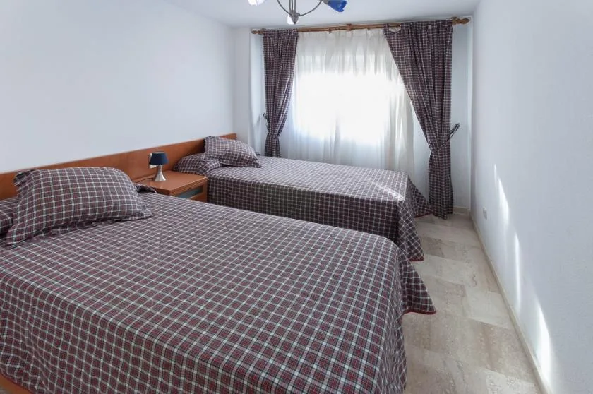 Un dormitorio con dos camas y una ventana luminosa enmarcada por cortinas.