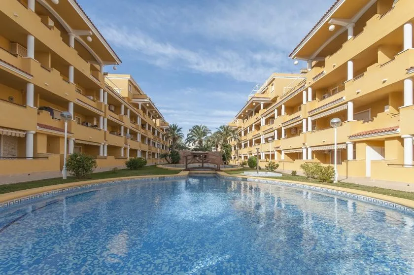 A swimming pool sits between rows of yellow apartment buildings.