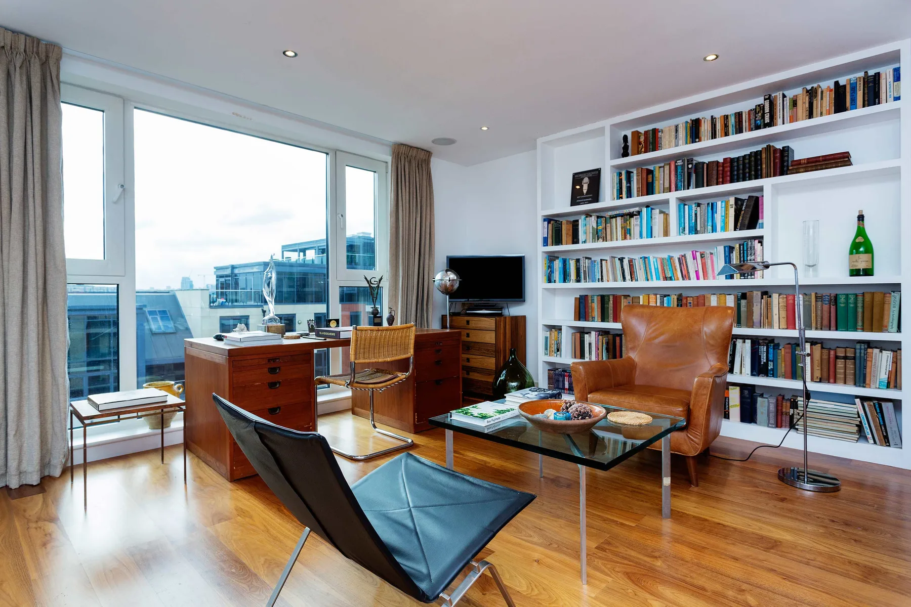 Una sala luminosa con una gran estantería y asientos junto a amplias ventanas.