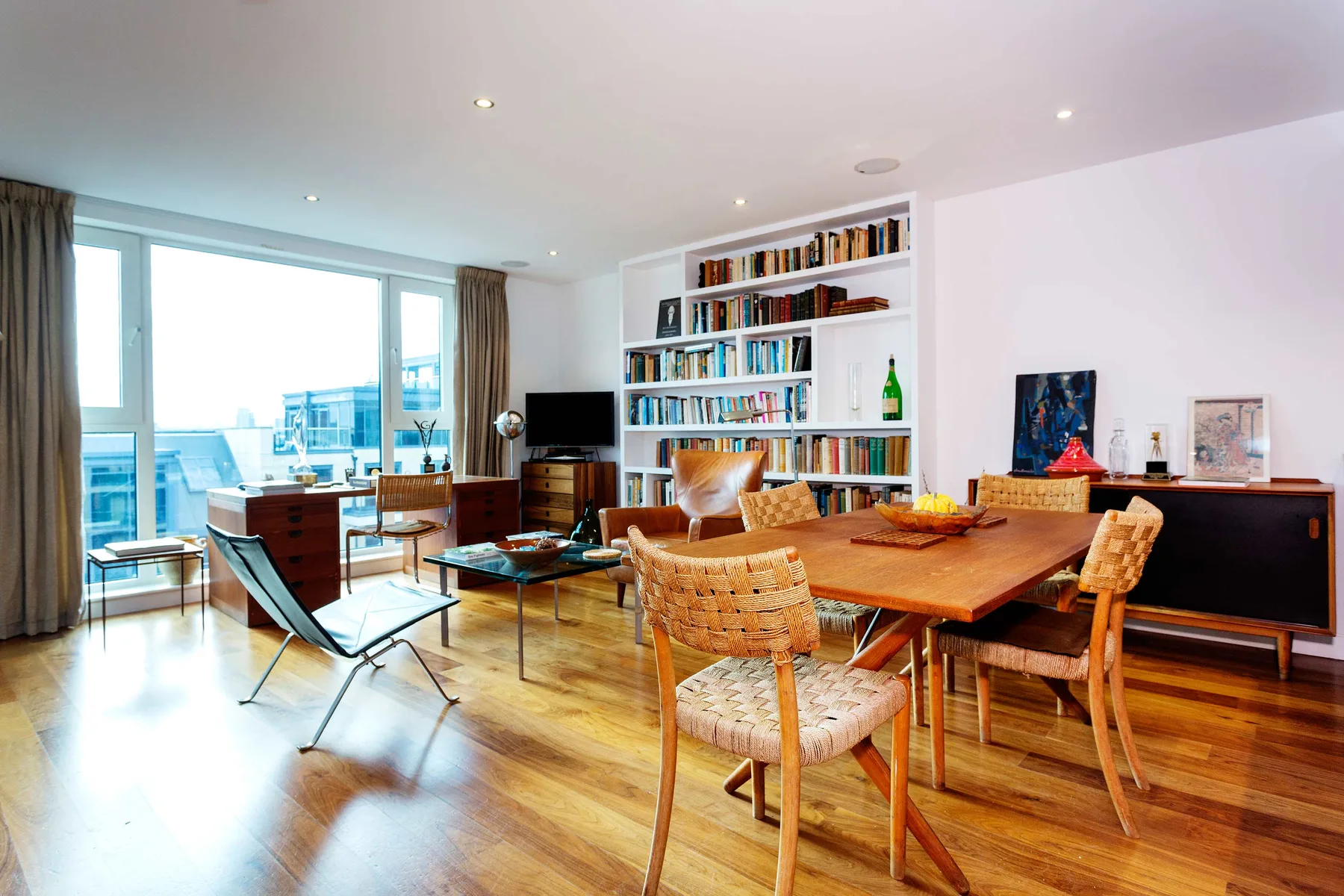 Una luminosa sala de estar y comedor con una mesa de madera y estanterías.