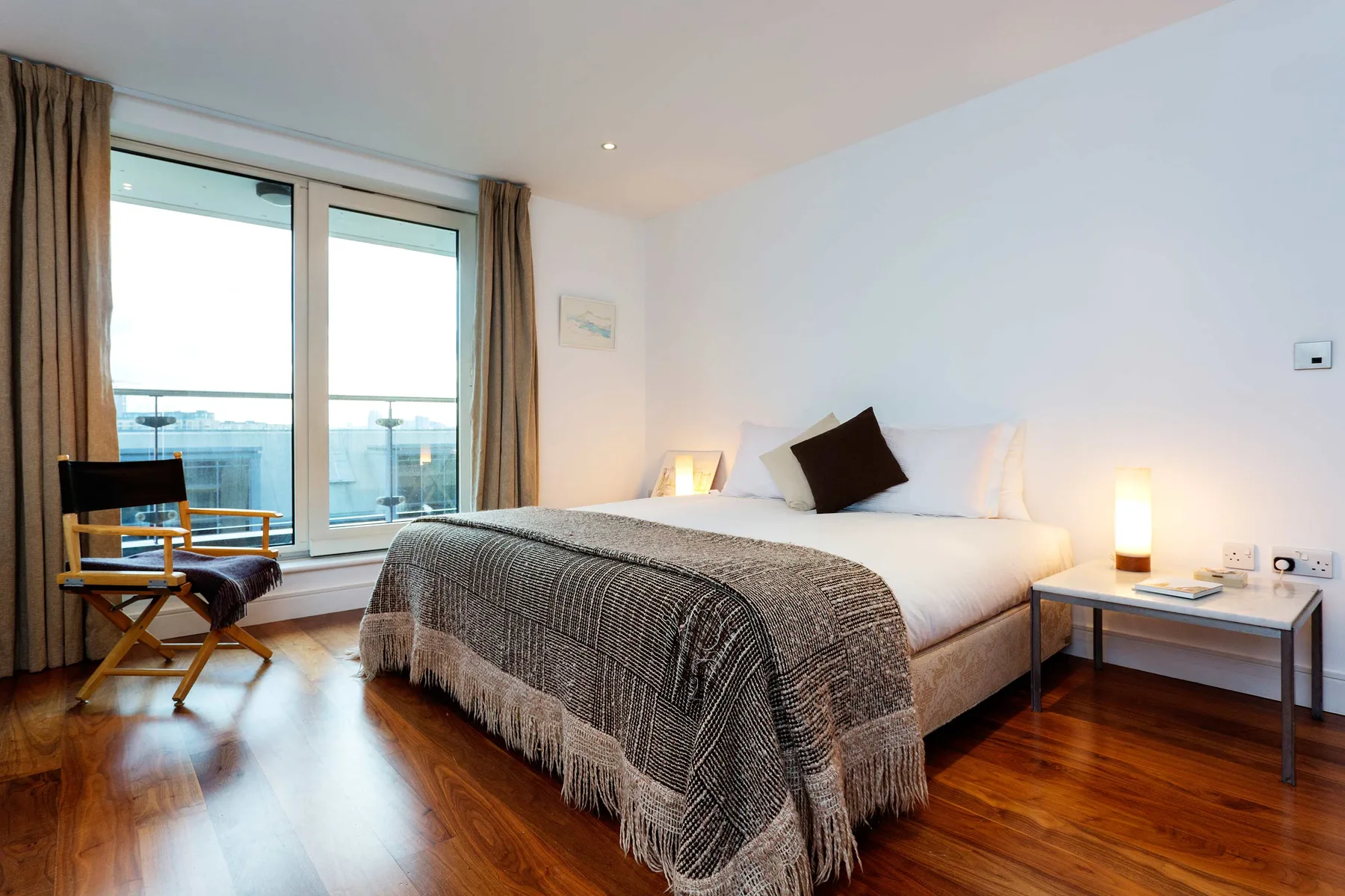Un dormitorio luminoso con una cama, ventanales y suelo de madera.