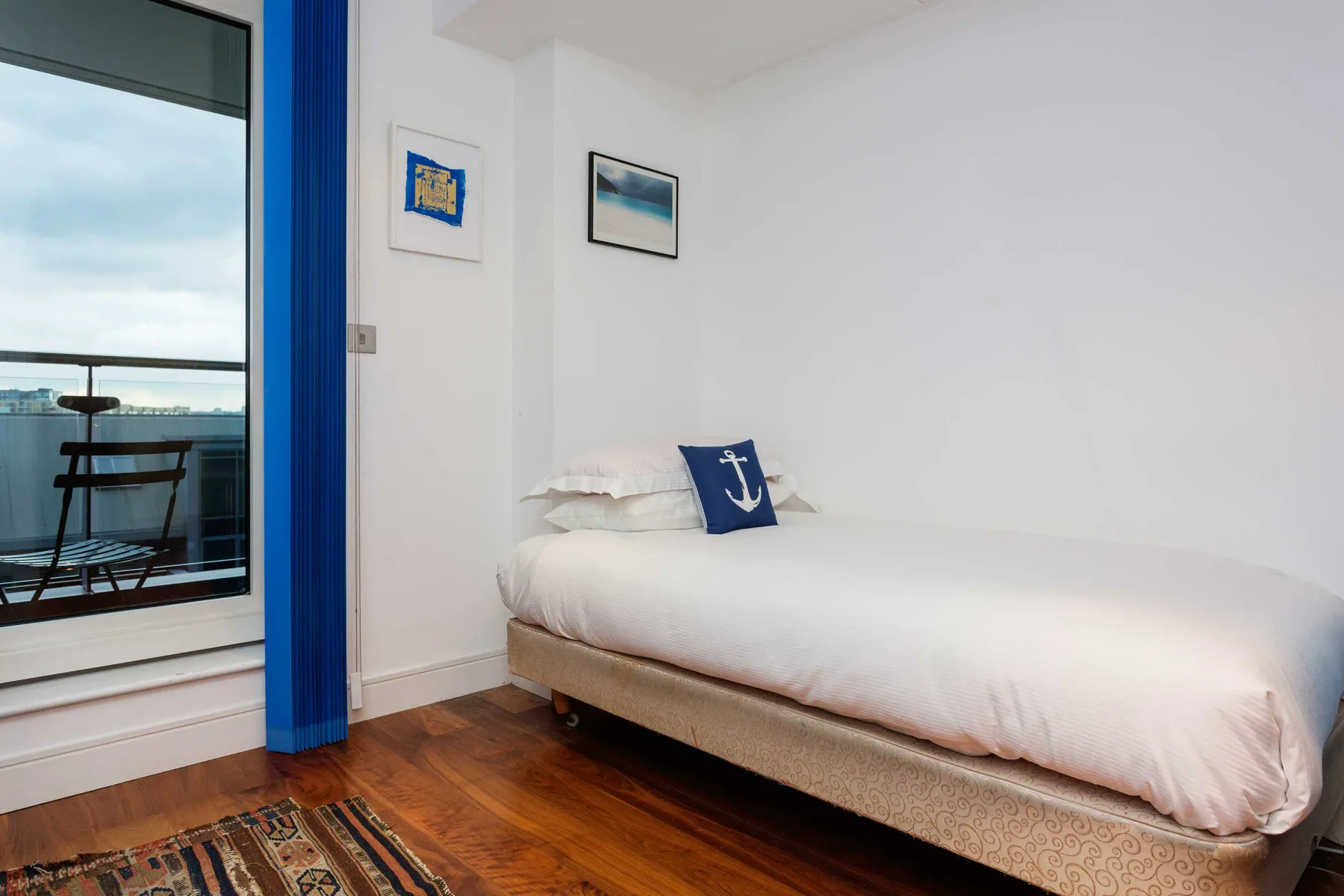 Un dormitorio luminoso con una cama blanca junto a una ventana grande.