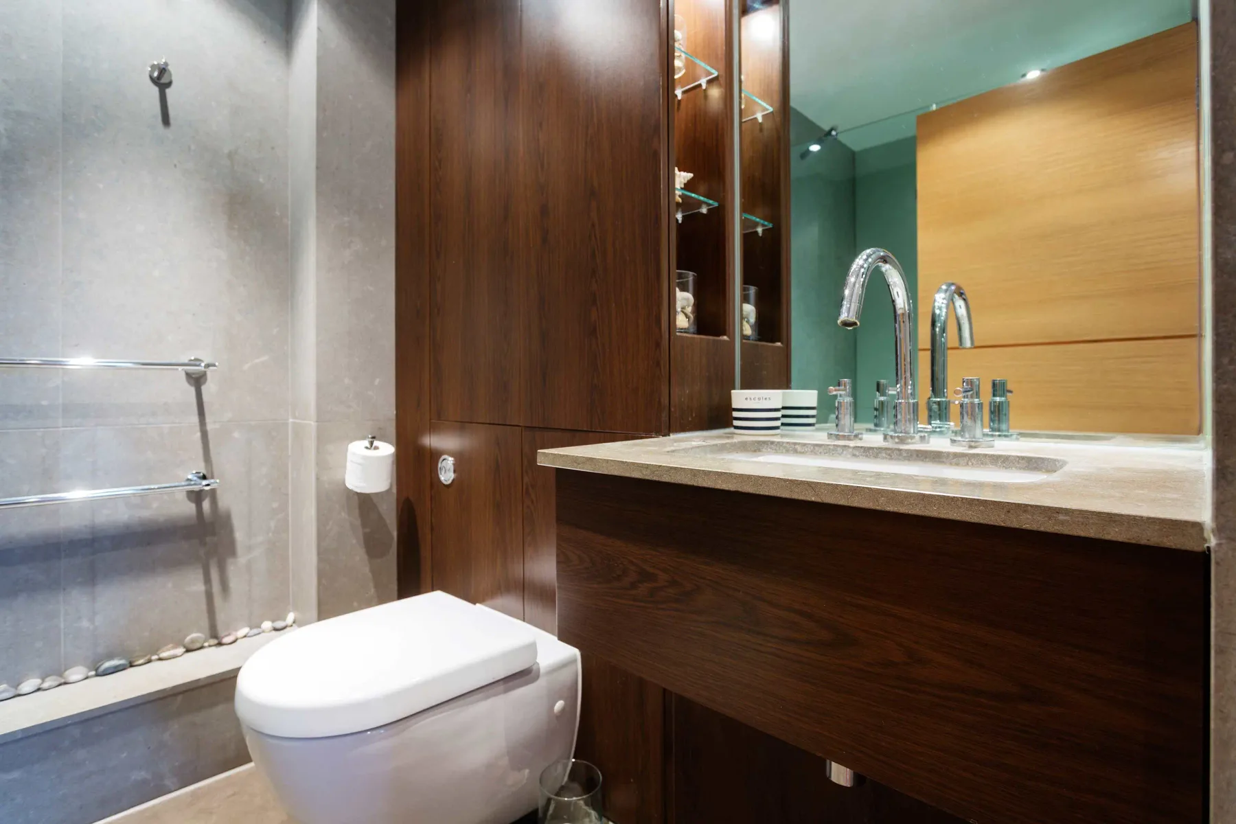 Un baño con inodoro, ducha de vidrio y mueble de madera junto al lavabo.