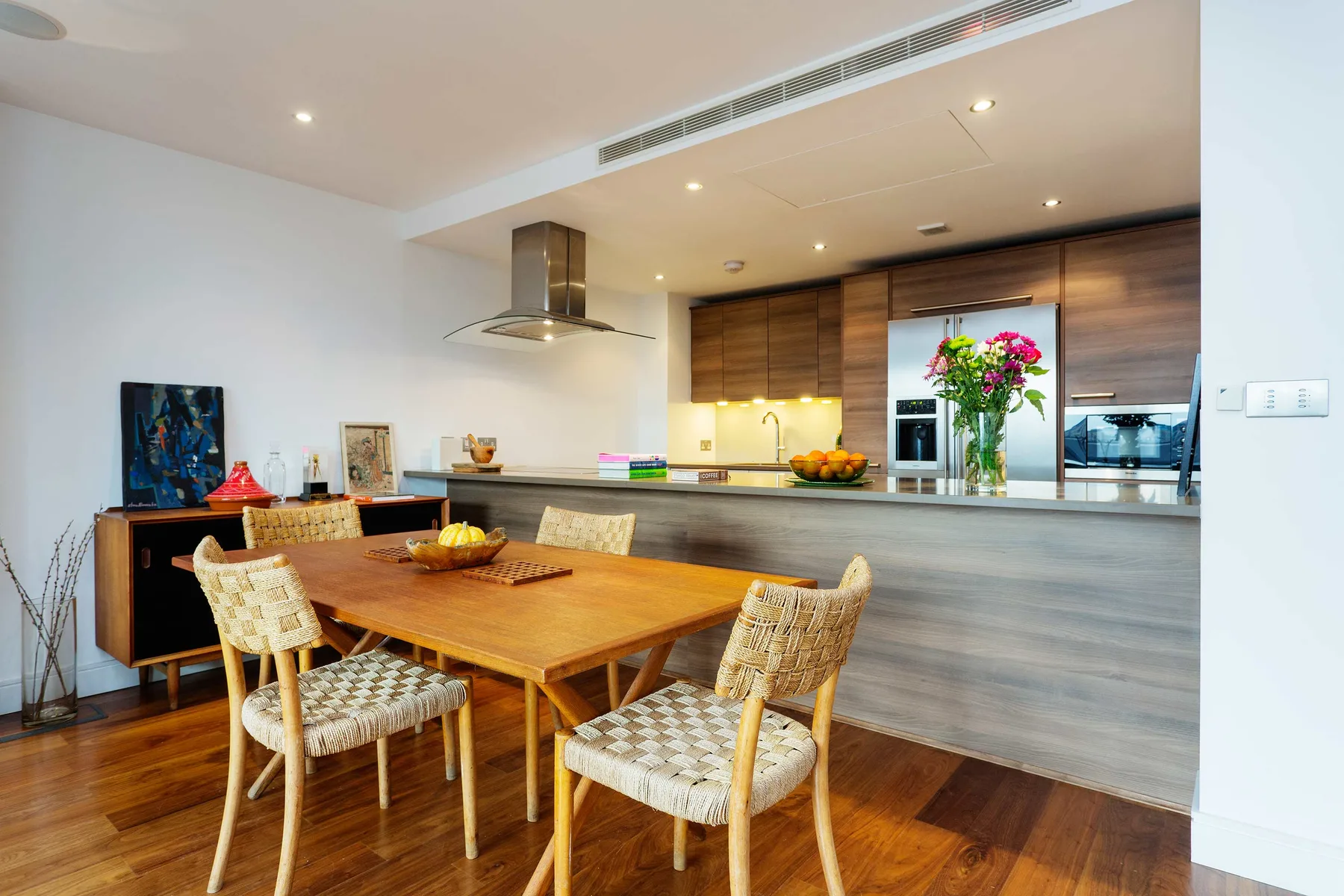 Comedor con mesa de madera y asientos tejidos junto a una cocina abierta.