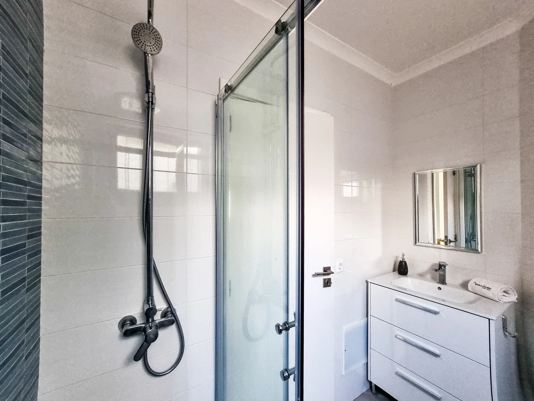 A tiled bathroom with a glass shower and white sink cabinet.