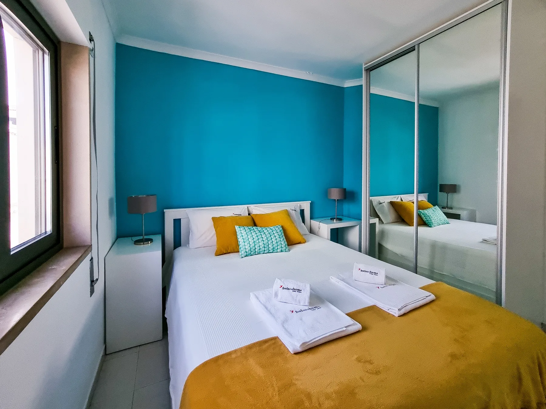 A bedroom with a white bed, mustard-colored bedding, and mirrored wardrobe doors.