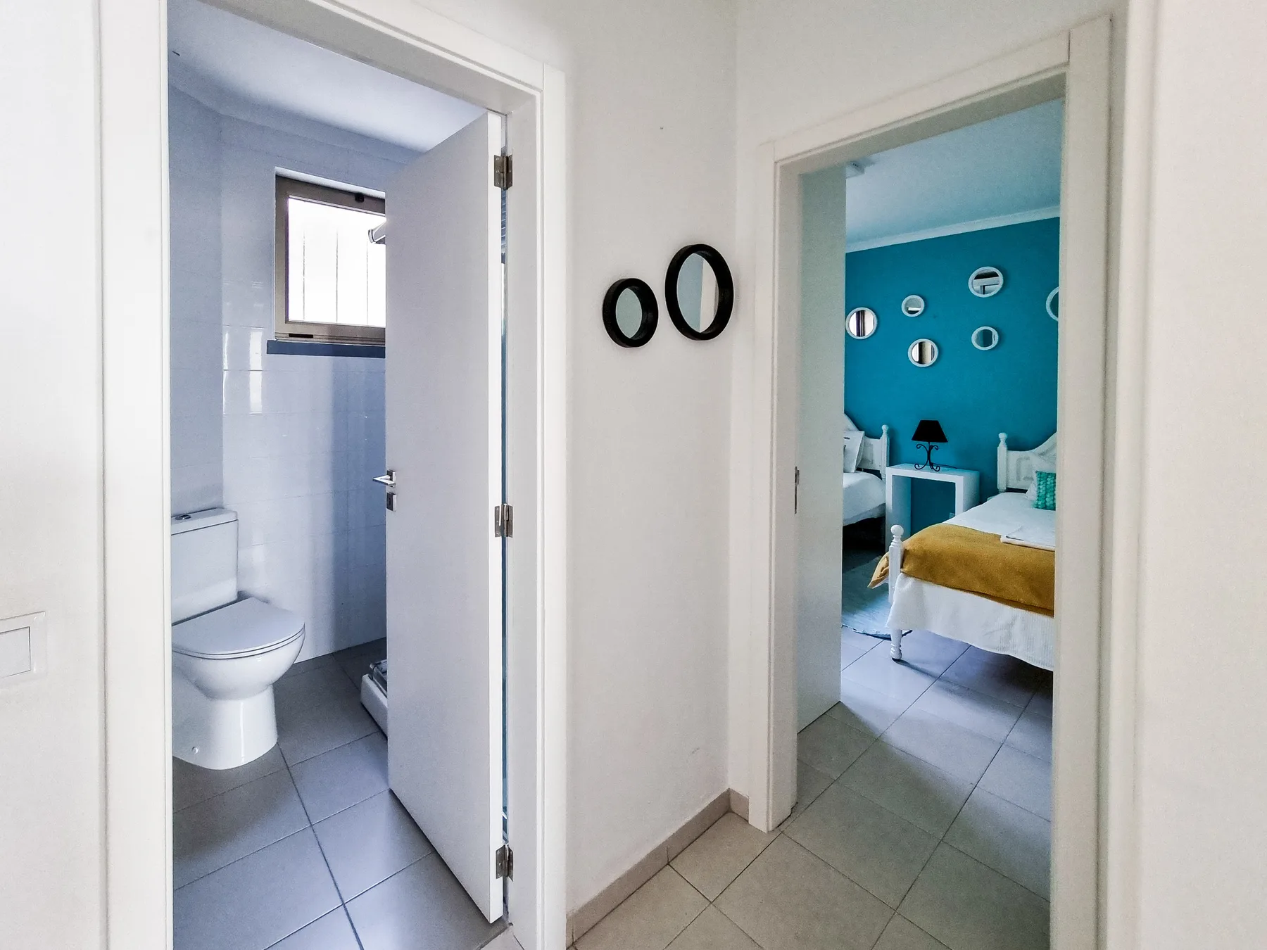 A hallway opens onto a bathroom and a bedroom with a bright blue wall.