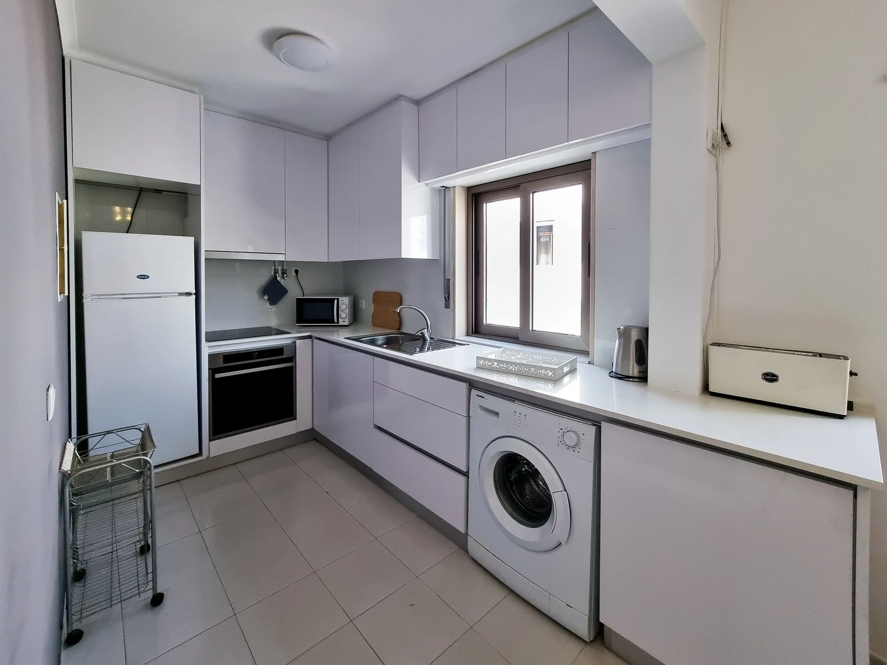 Una cocina compacta con armarios claros, electrodomésticos y una ventana sobre la encimera.