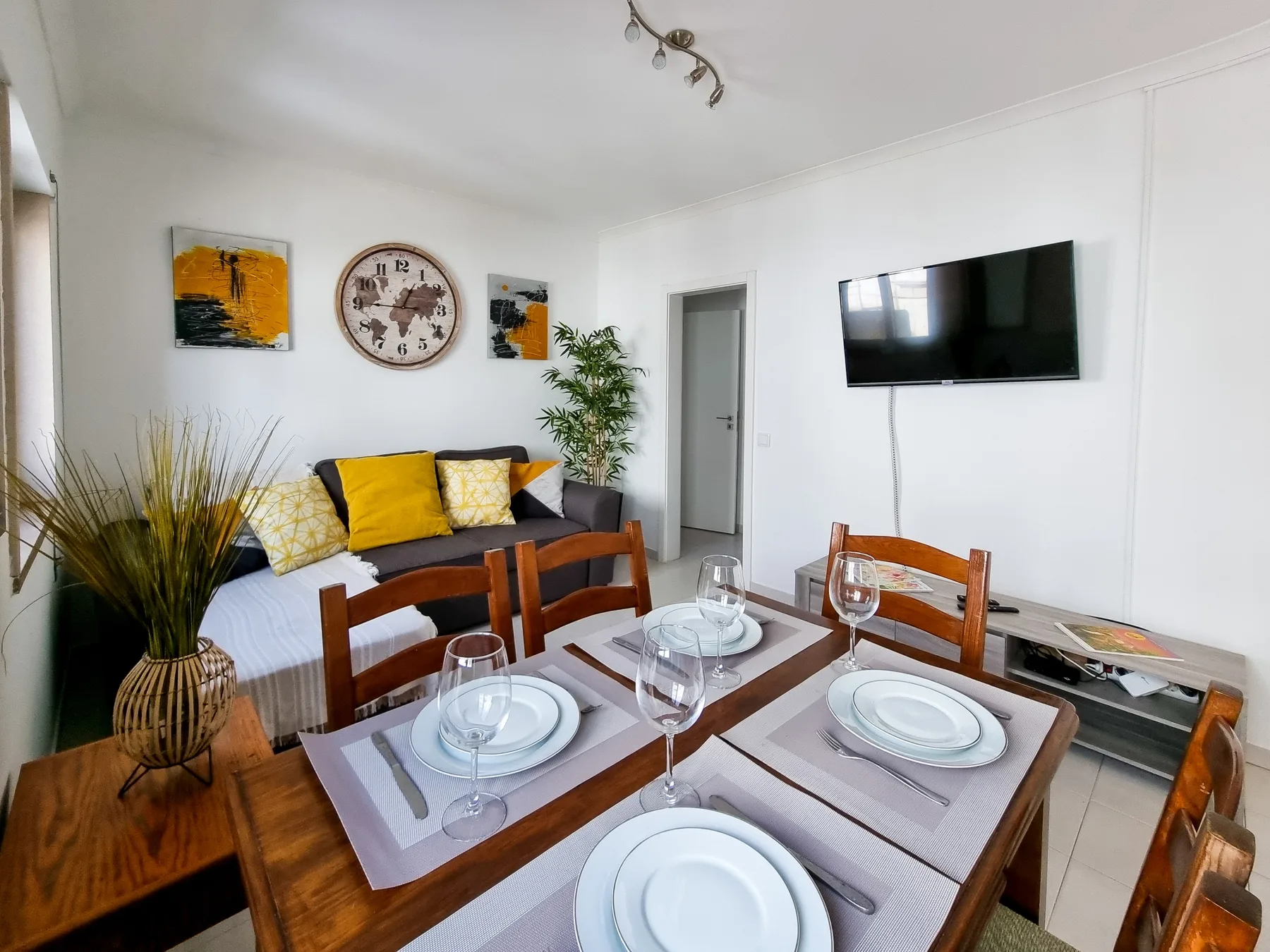A dining and living area with a set table, seating, and a wall-mounted television.
